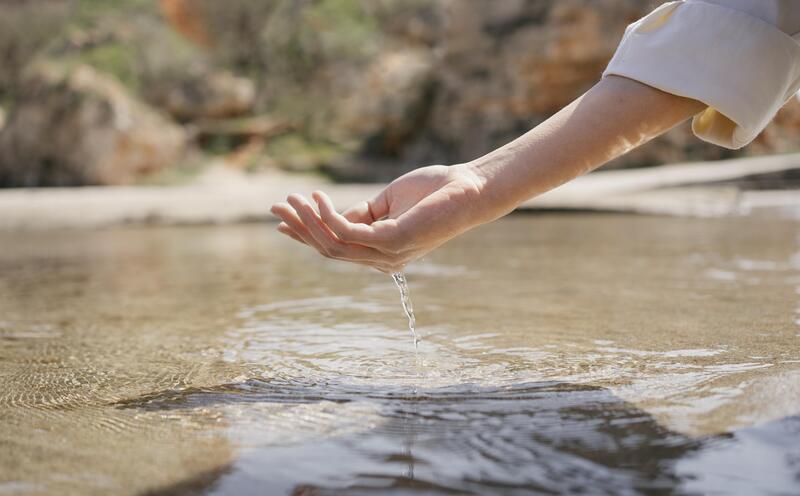 Mano cogiendo agua en un entorno rural